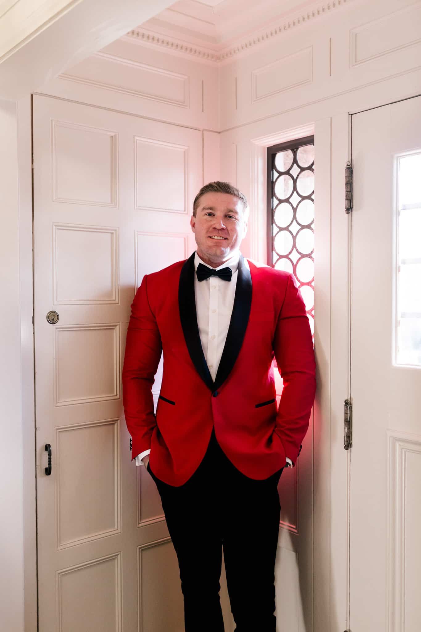 A man in a red tuxedo and bow tie is standing in front of a door.