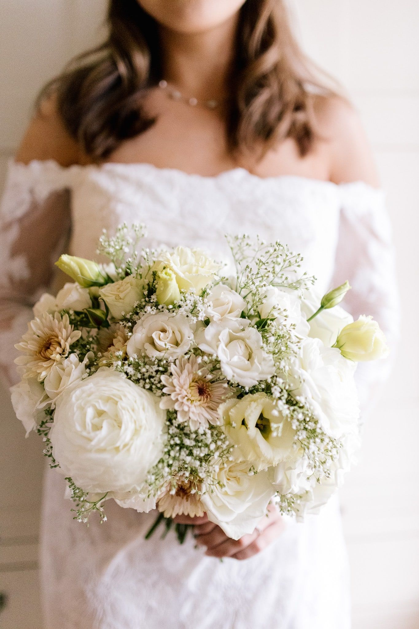 A woman in a white dress is holding a bouquet of white flowers.