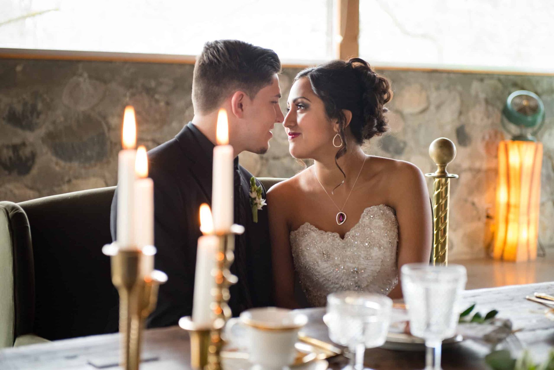 A bride and groom are sitting at a table with candles and looking at each other.