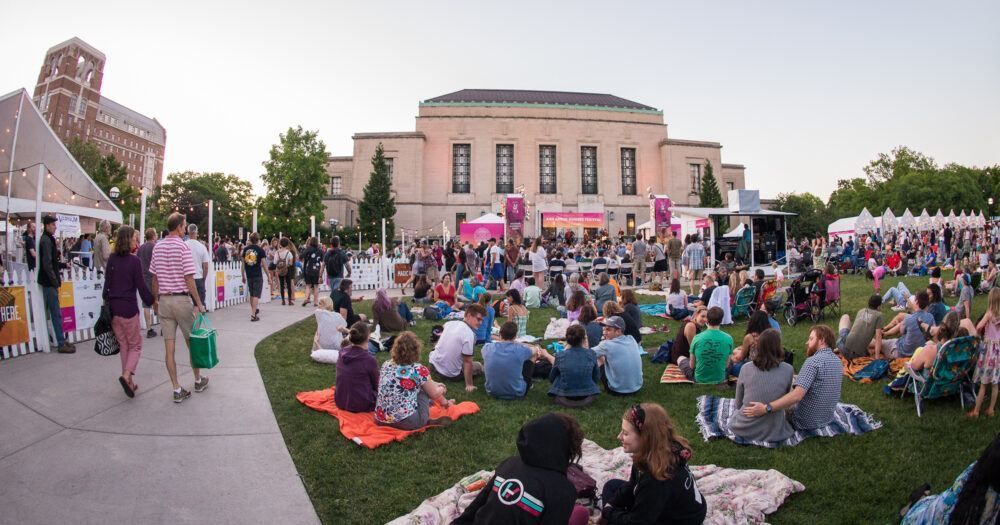 A large group of people are sitting on the grass in front of a large building.