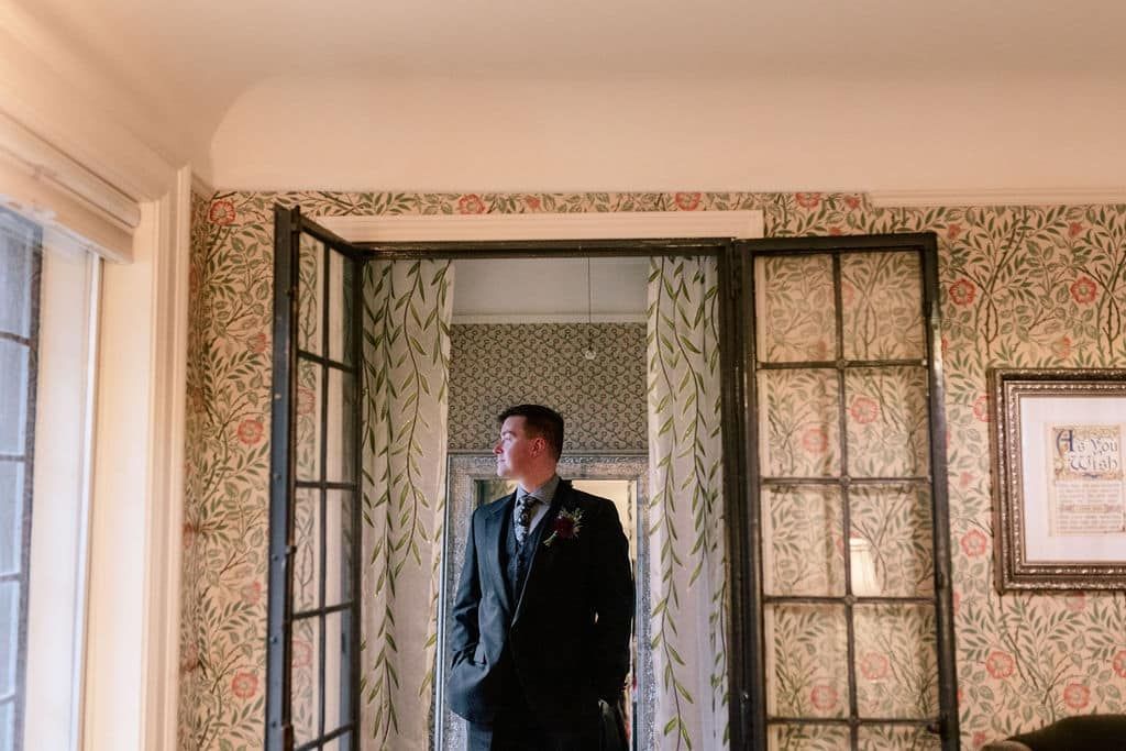 A man in a suit and tie is standing in a room next to a window.