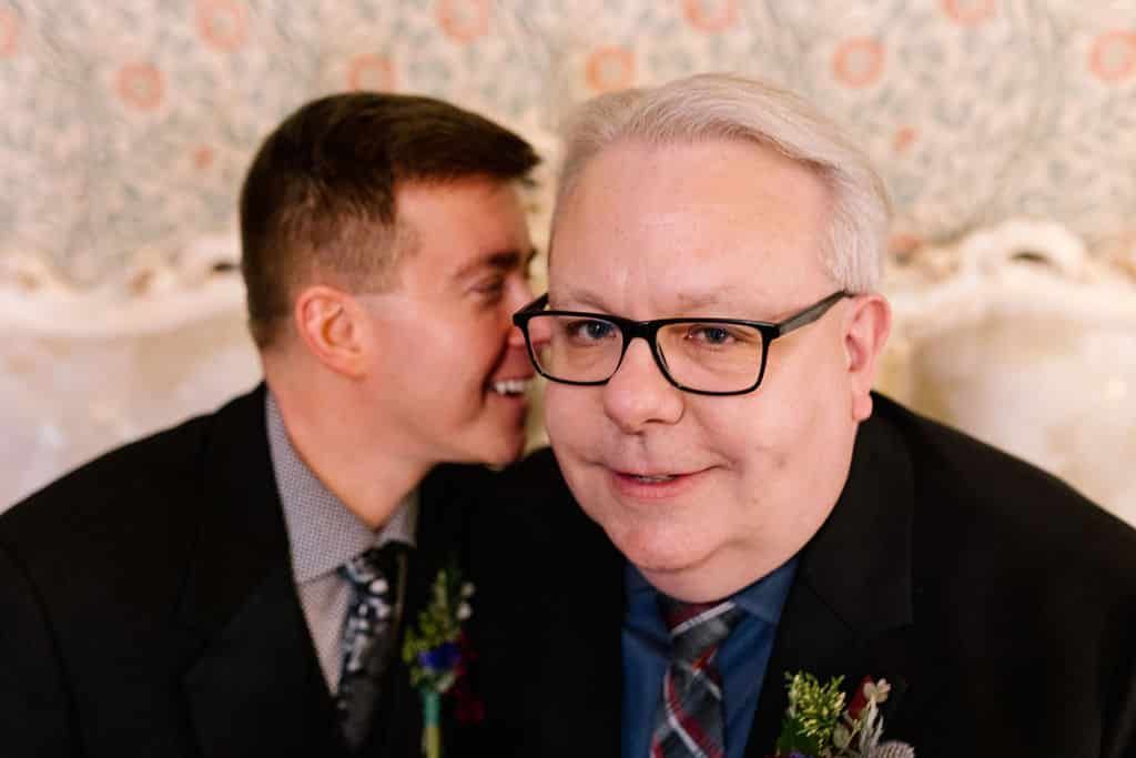 A man is whispering into another man 's ear.