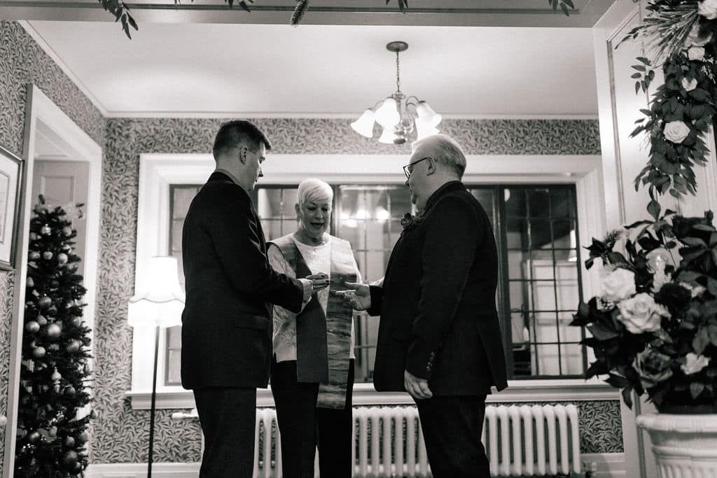 Three men in suits are shaking hands in a living room.