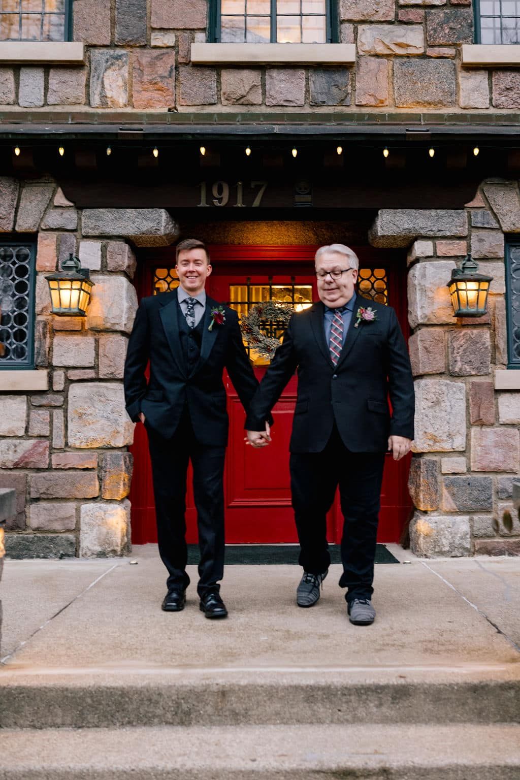 Two men in suits are holding hands in front of a building.