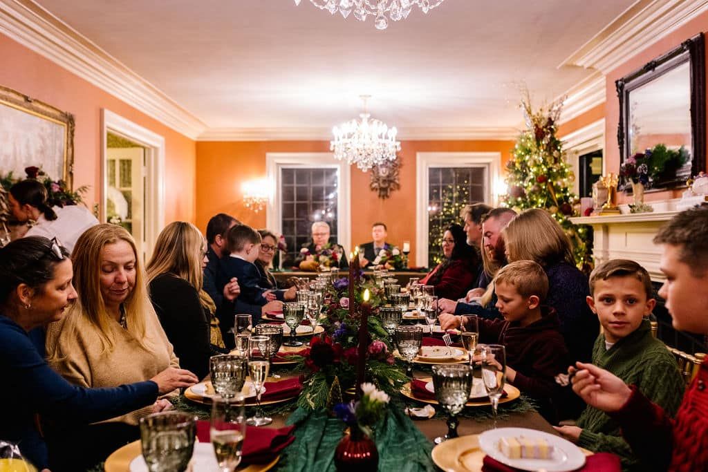 A large group of people are sitting at a long table eating christmas dinner.