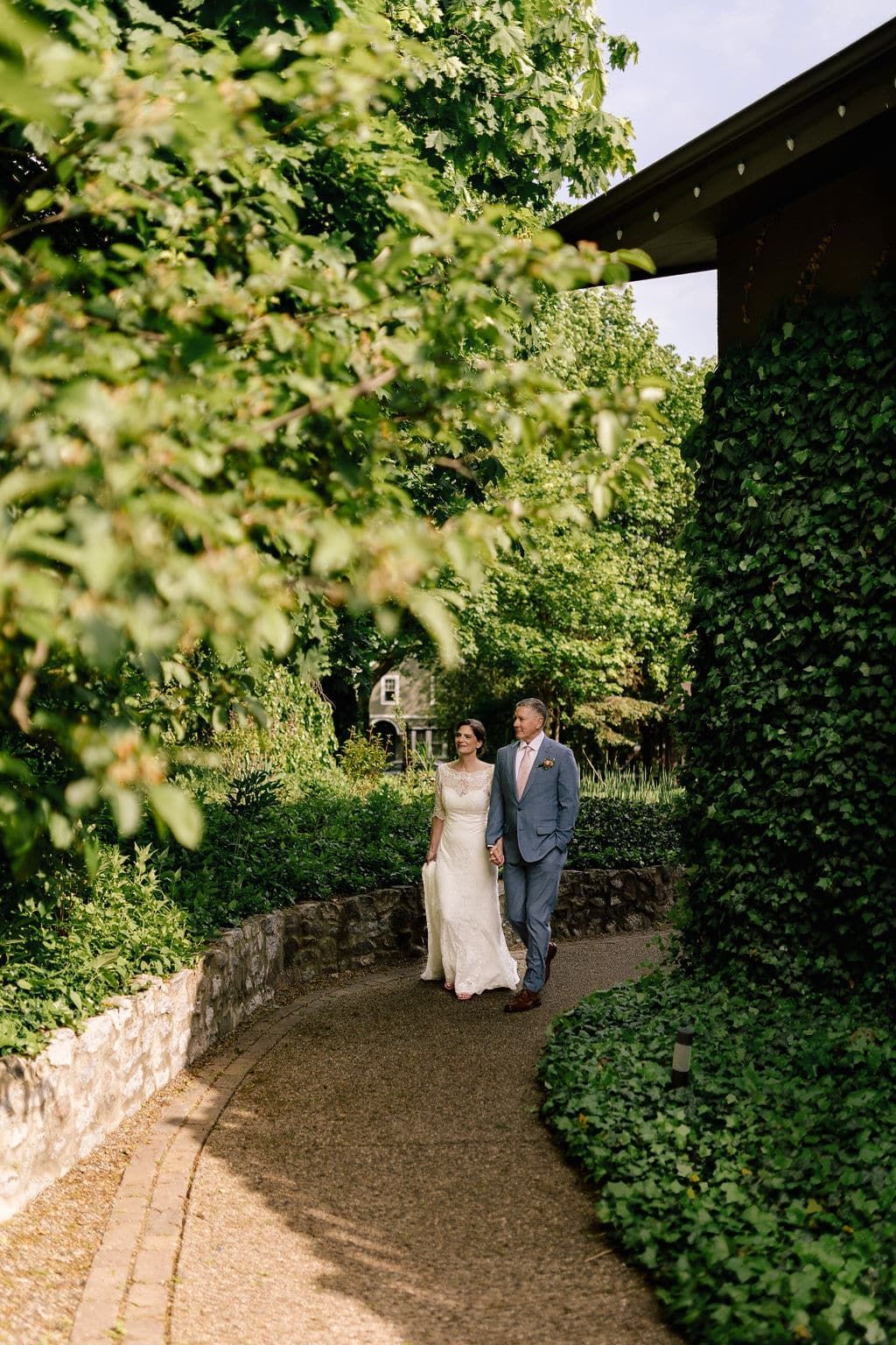 A bride and groom are walking down a path surrounded by trees.