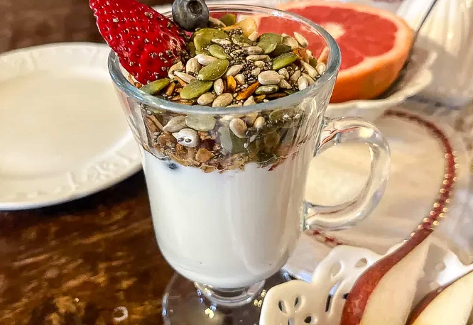 A glass of yogurt with granola and strawberries on a table.