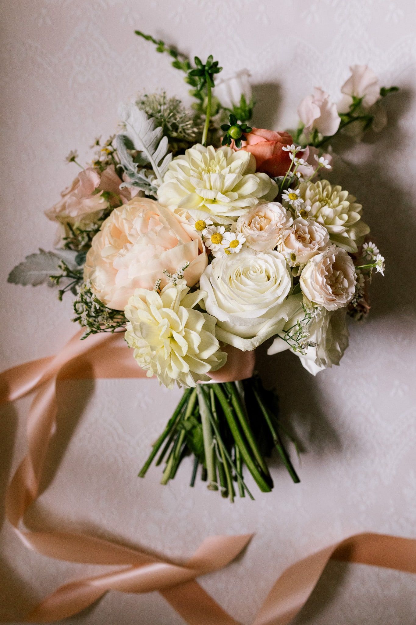A bouquet of flowers with a pink ribbon is hanging on a wall.