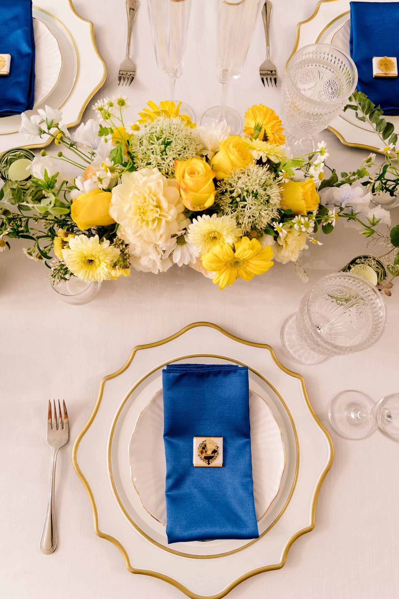 A table setting with plates , napkins , glasses and a vase of flowers.