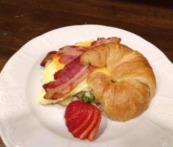 Breakfast sandwich on croissant with bacon, egg, and cheese, served with a sliced strawberry.