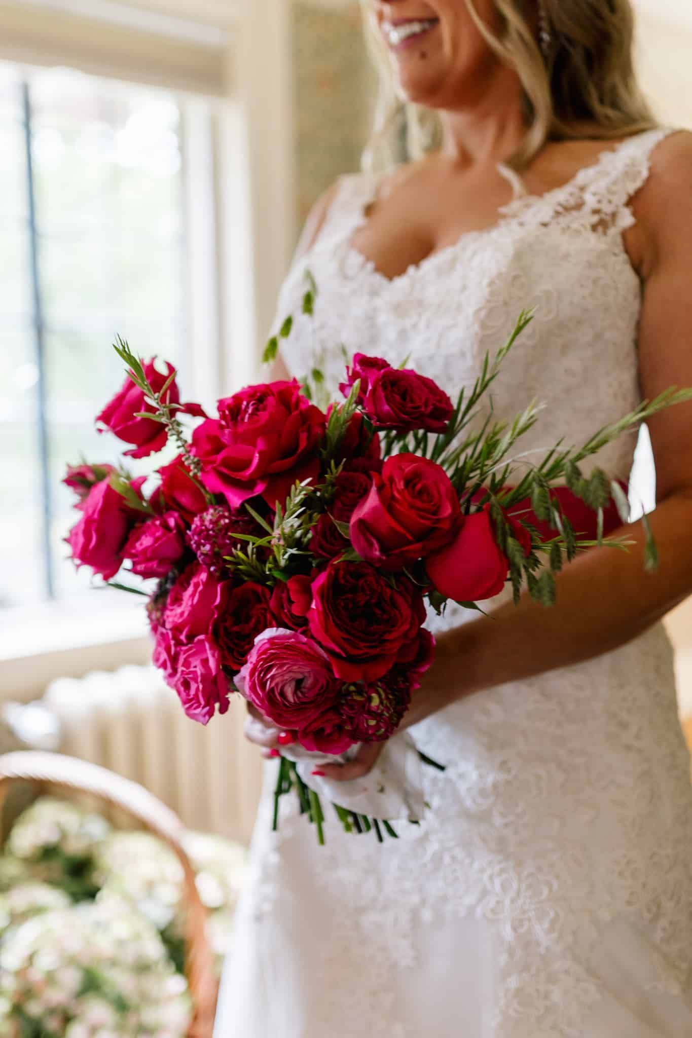 A bride in a white dress is holding a bouquet of red roses.