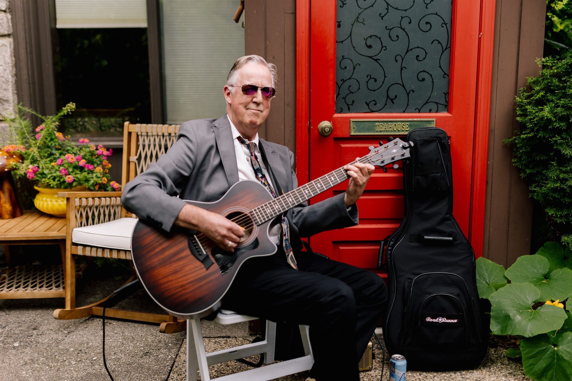 A man is sitting in a chair playing a guitar in front of a red door.
