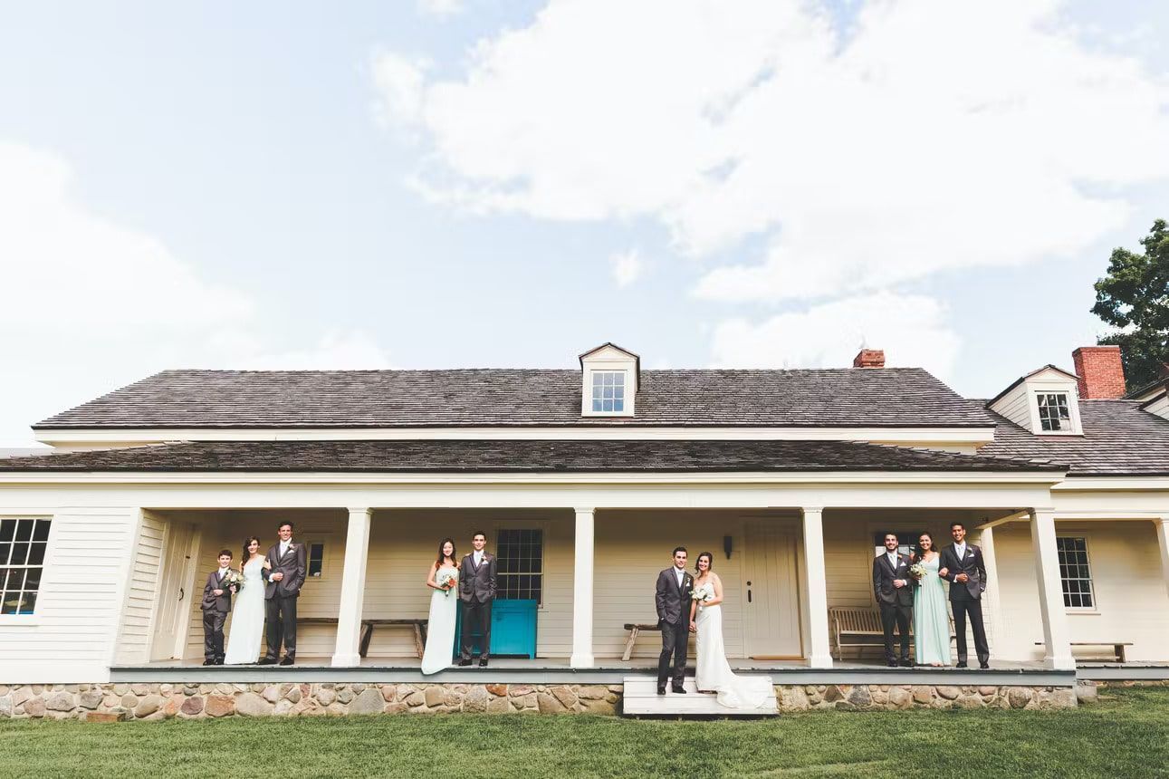 A bride and groom are posing for a picture with their wedding party on the porch of a house.