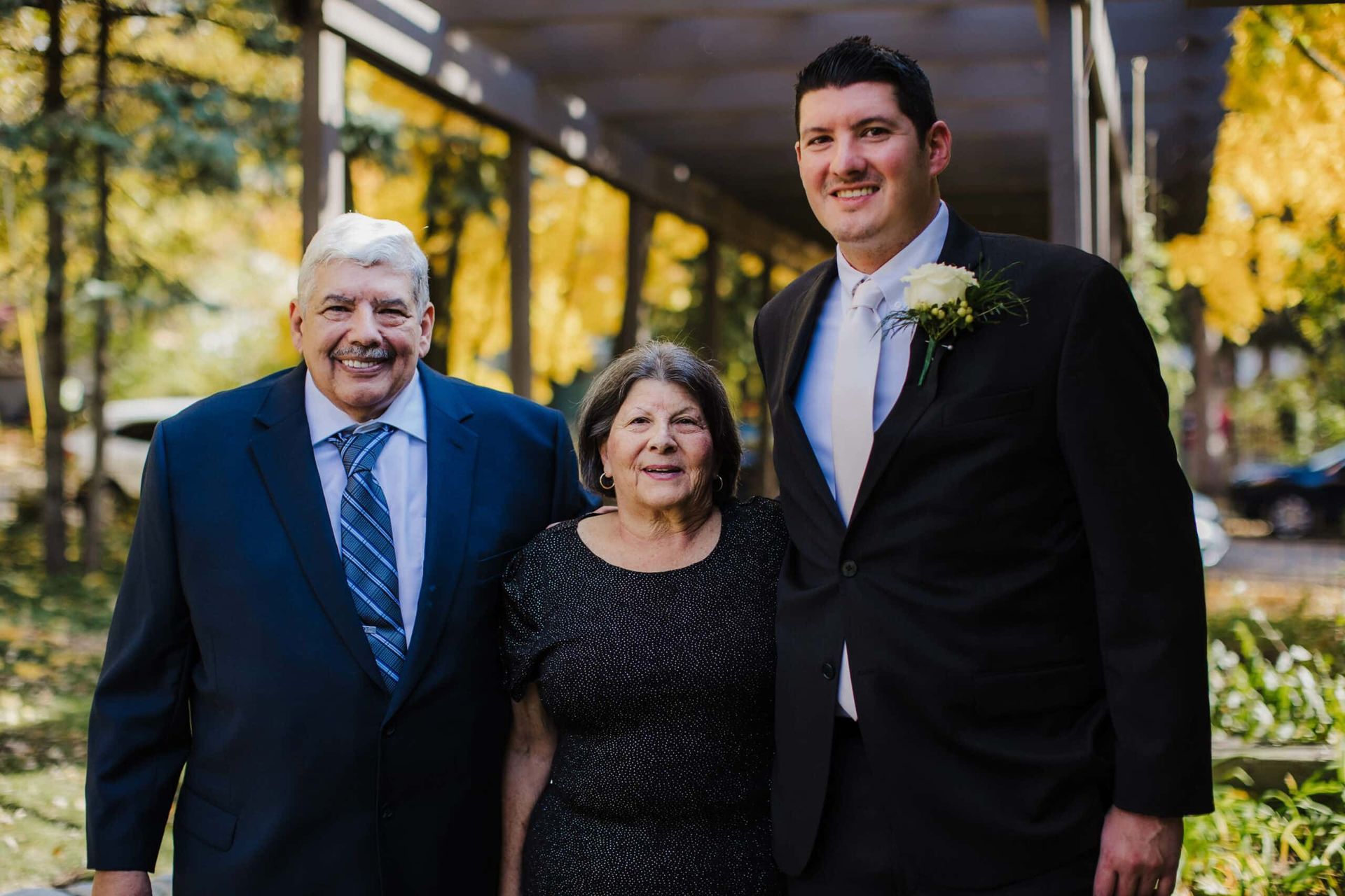 A man in a suit and tie is posing for a picture with his parents.
