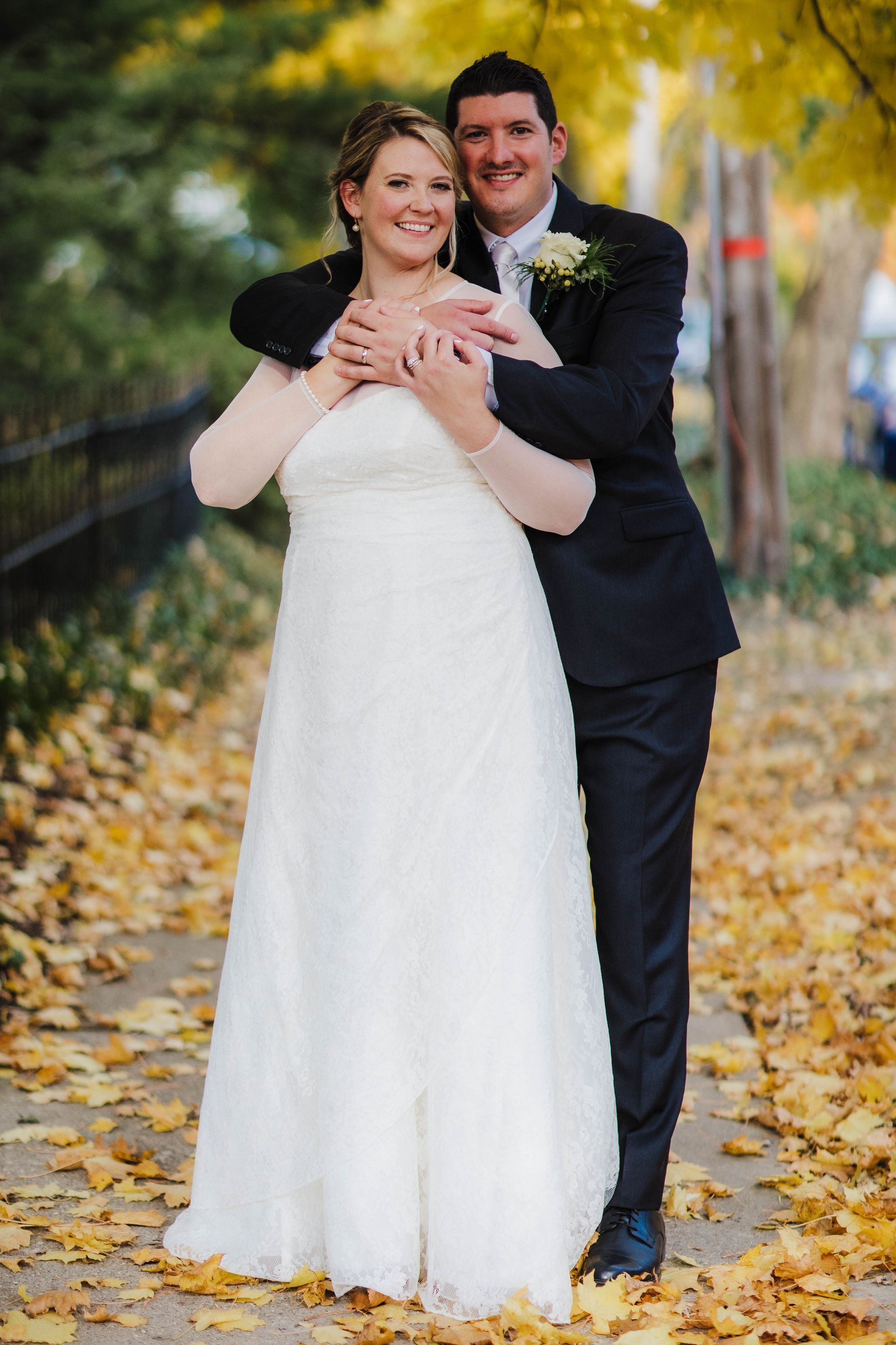 A bride and groom are posing for a picture in a park surrounded by leaves.