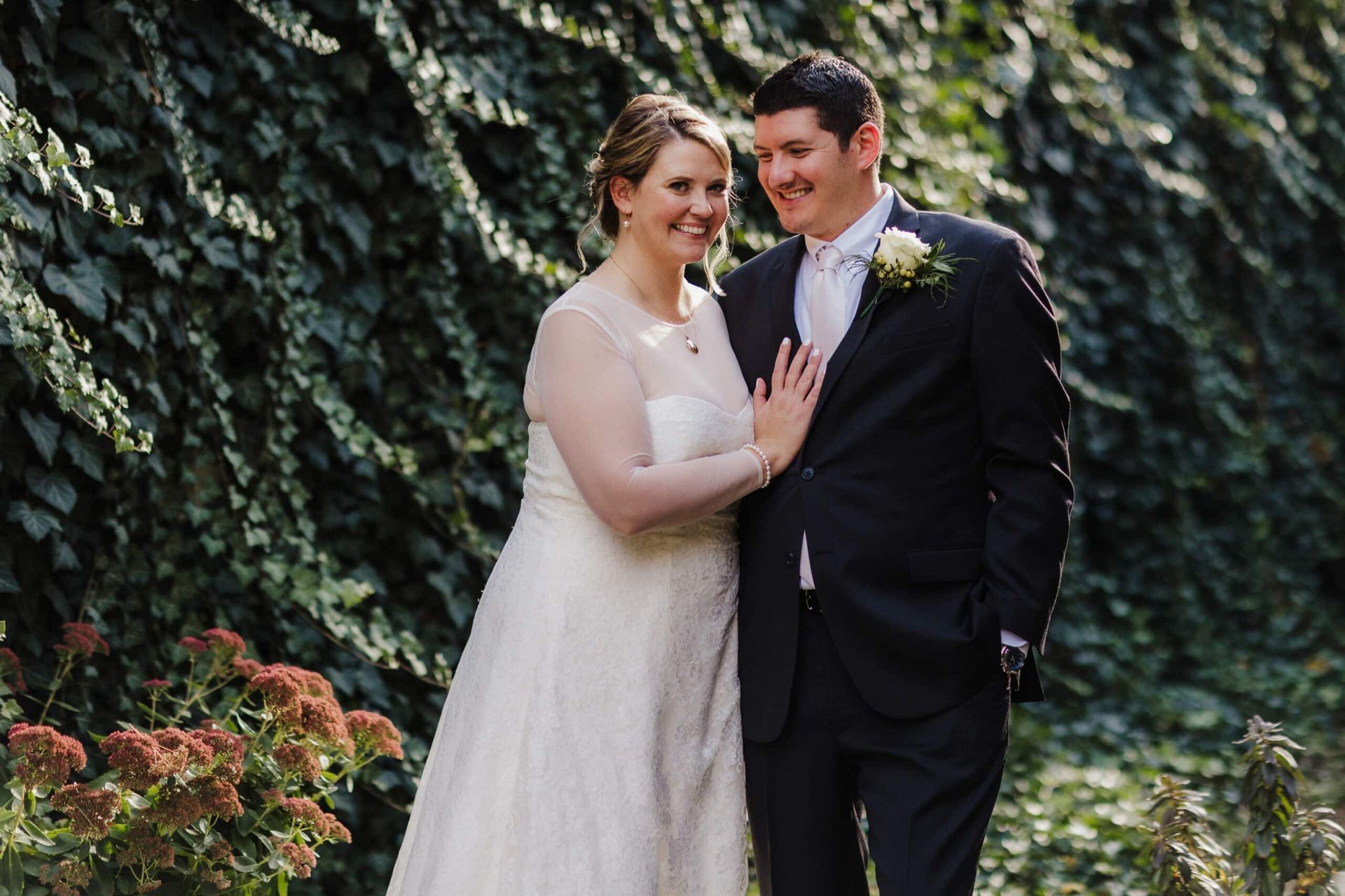 A bride and groom are posing for a picture in front of a bush.