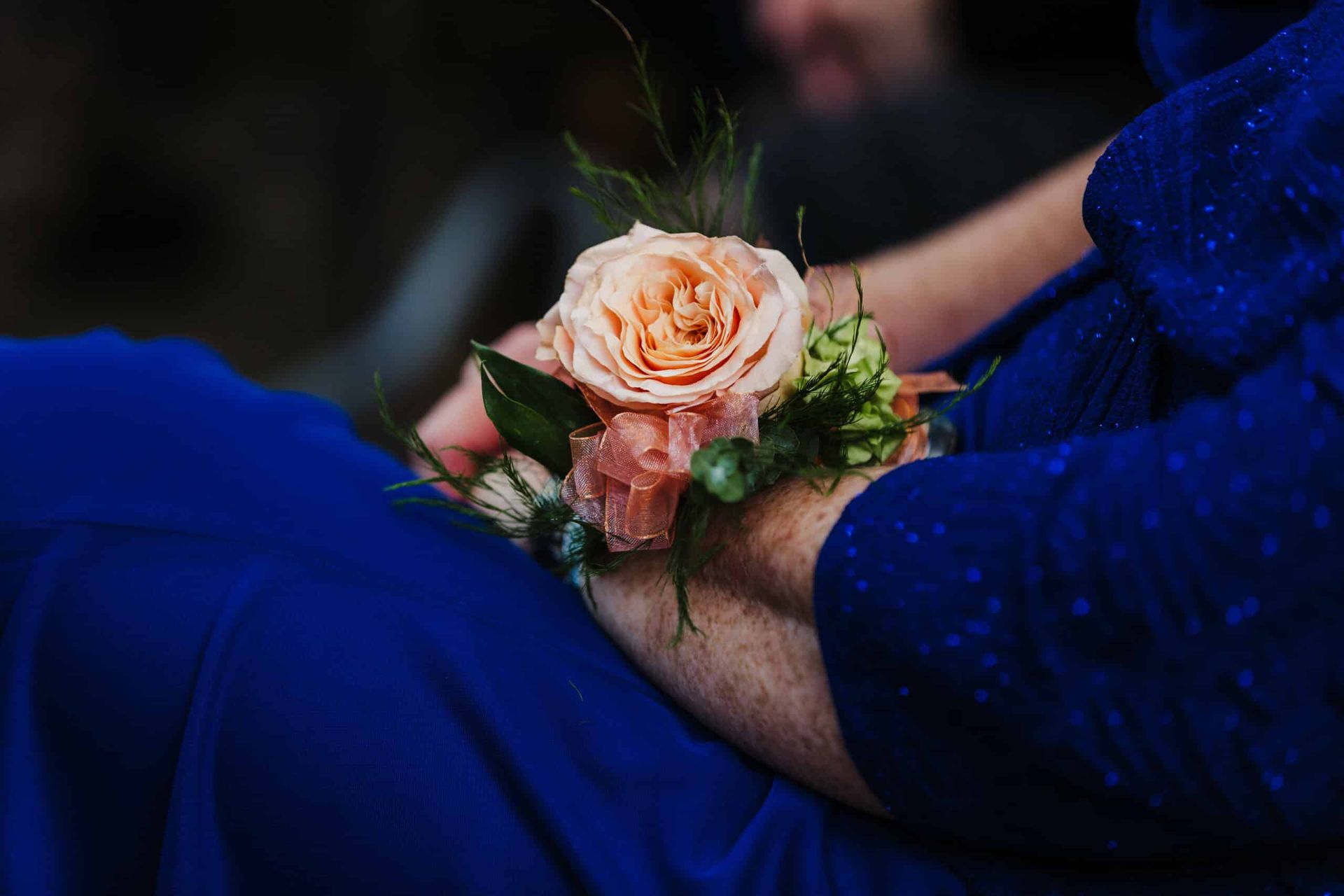 A woman in a blue dress is holding a bouquet of flowers on her wrist.