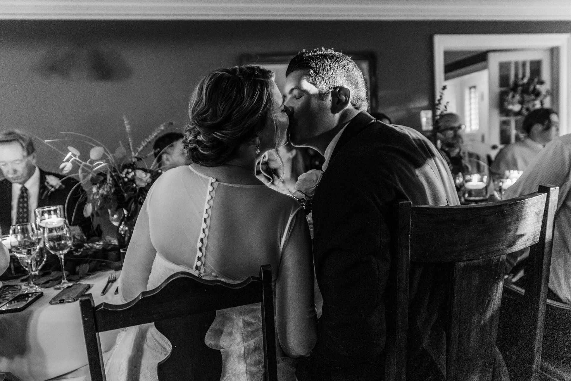 A black and white photo of a bride and groom kissing at their wedding reception.