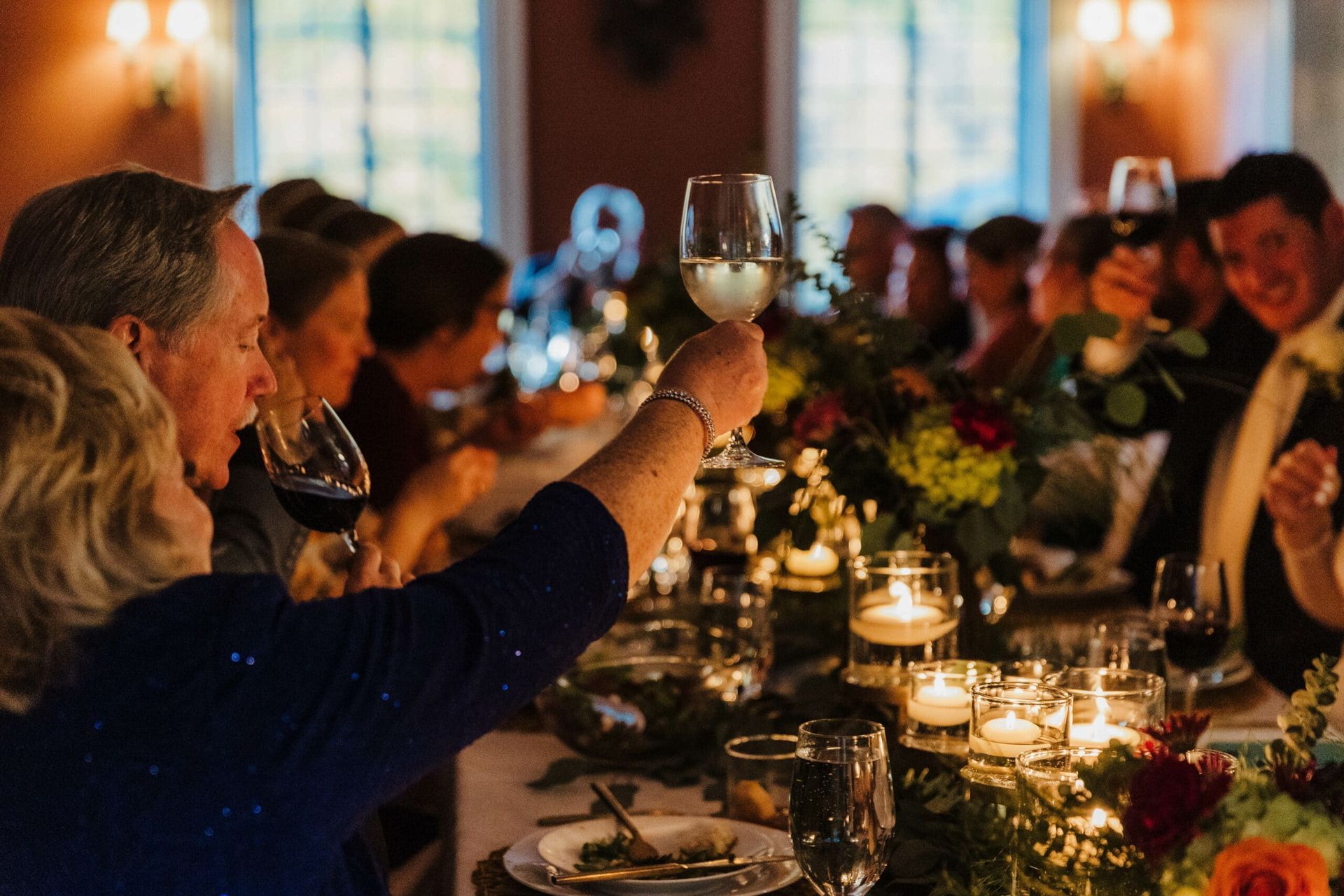 A group of people are sitting at a long table toasting with wine glasses.
