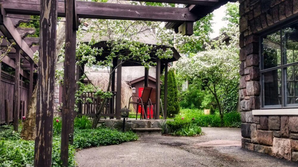 A stone building with a pergola and a red chair in front of it.