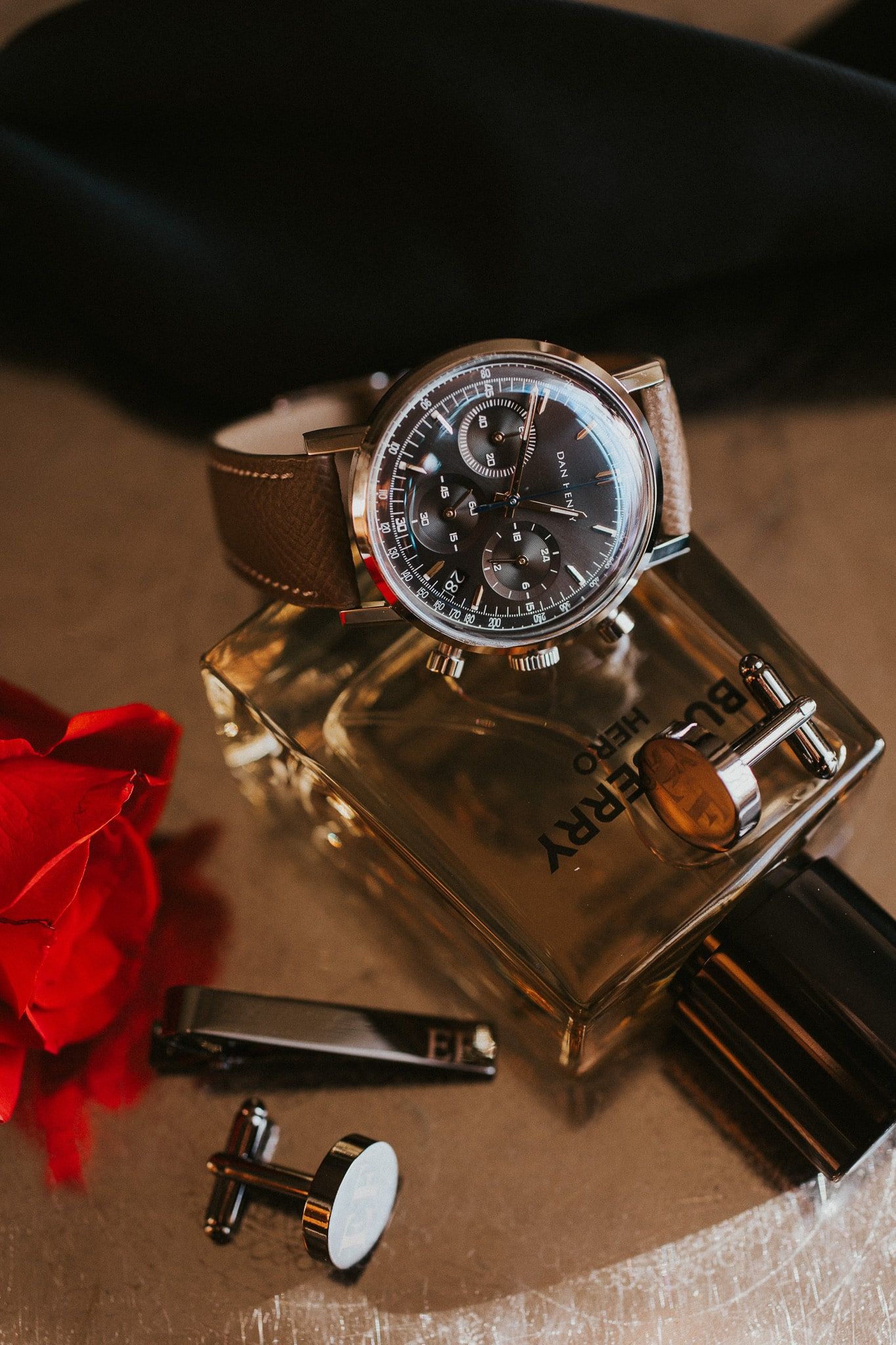 A watch is sitting on top of a bottle of burberry perfume.