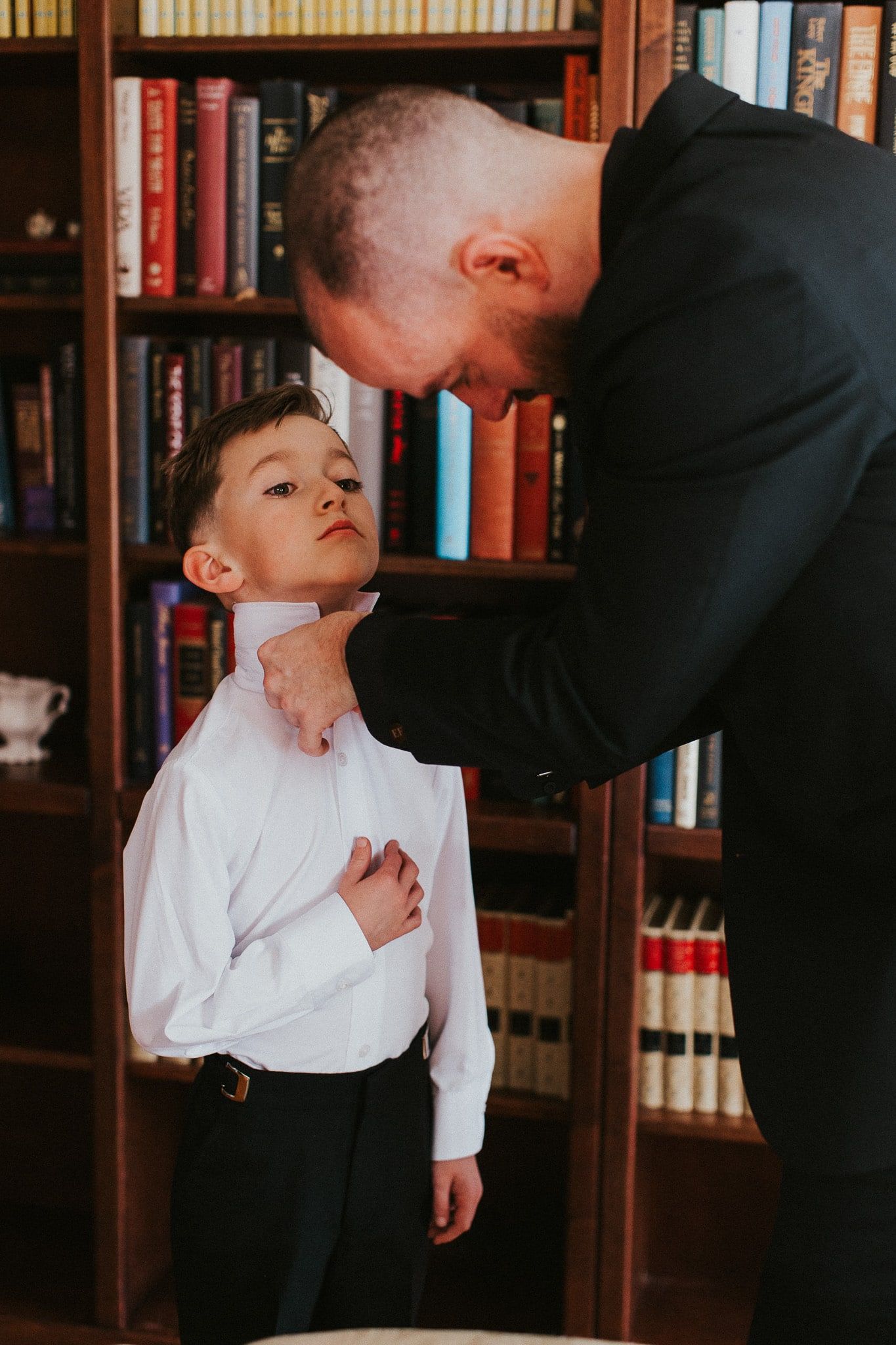 A man is adjusting a boy 's tie in front of a bookshelf.