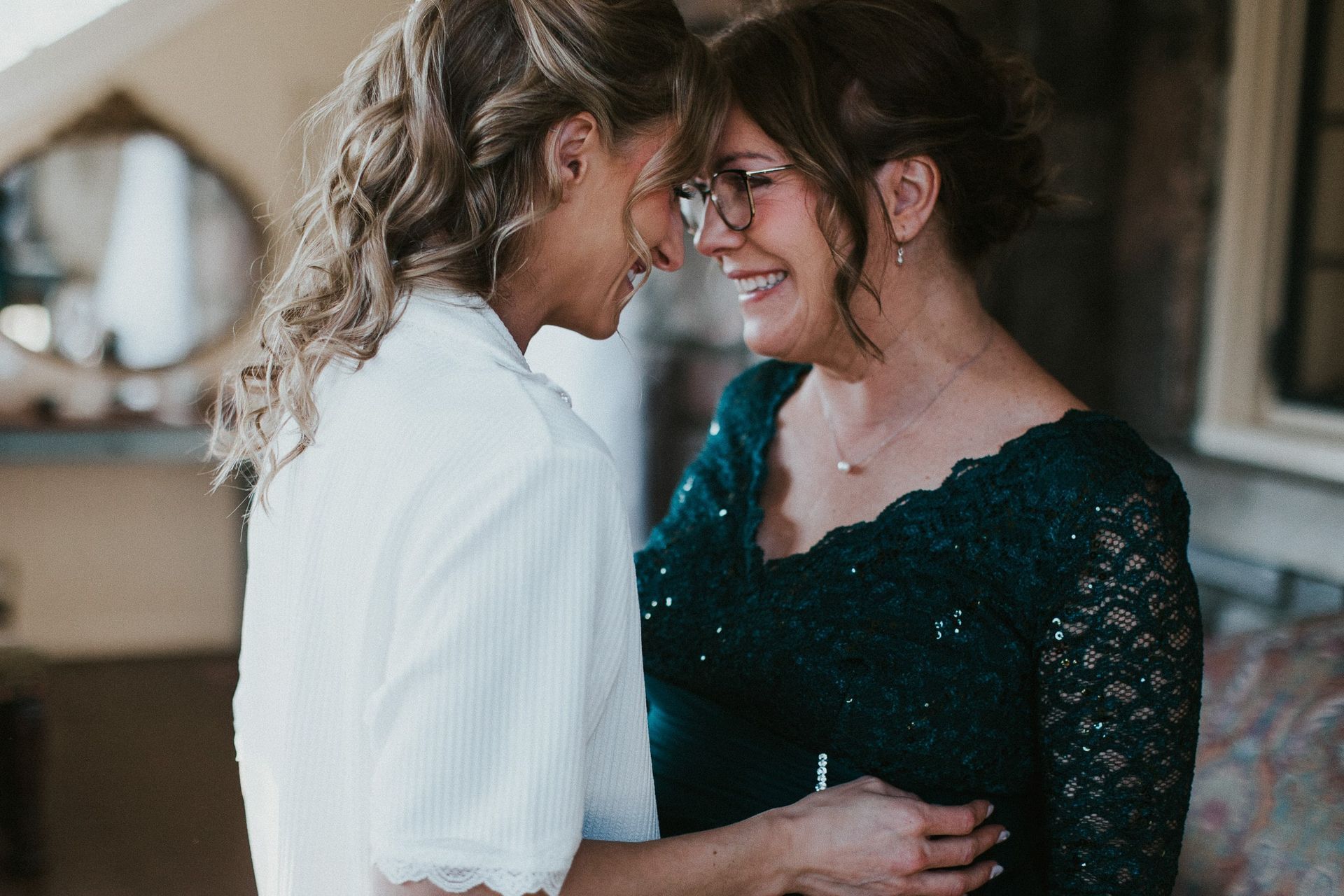 A bride and her mother are looking at each other and smiling.