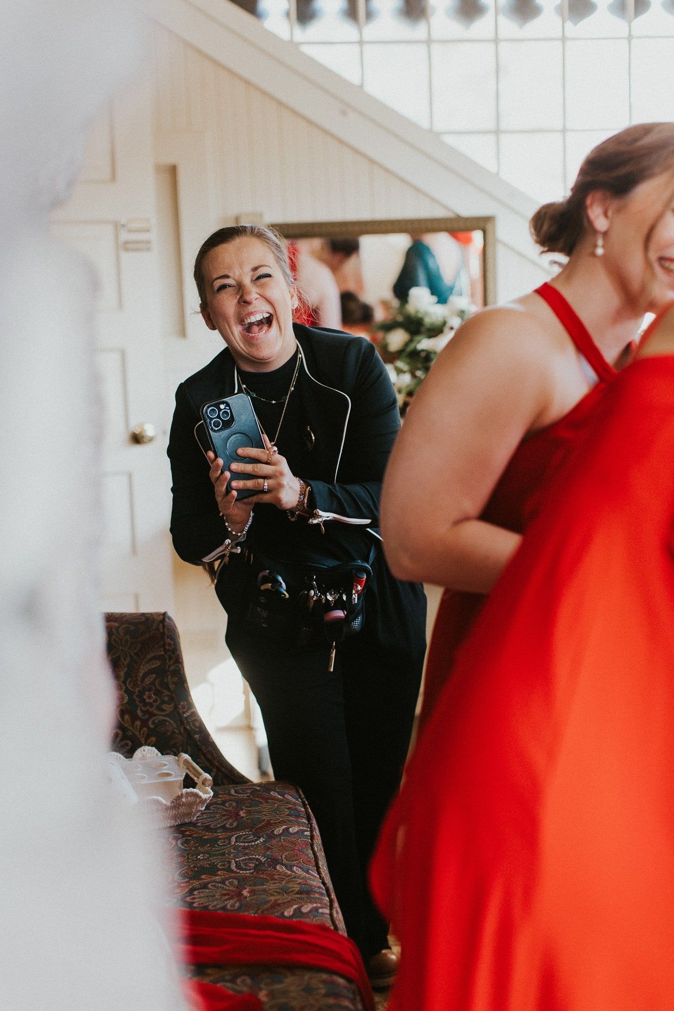 A woman in a red dress is laughing while another woman takes a picture of her.