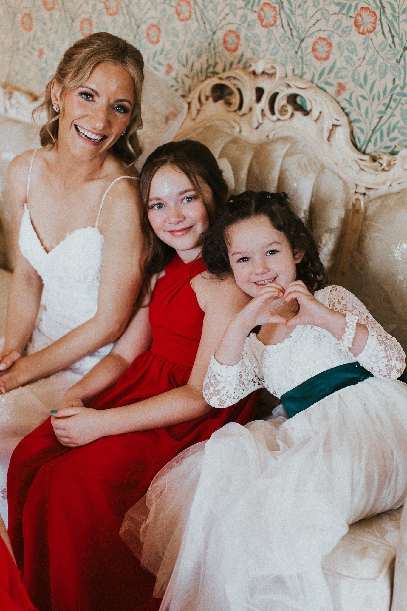 A bride and her two flower girls are sitting on a couch.