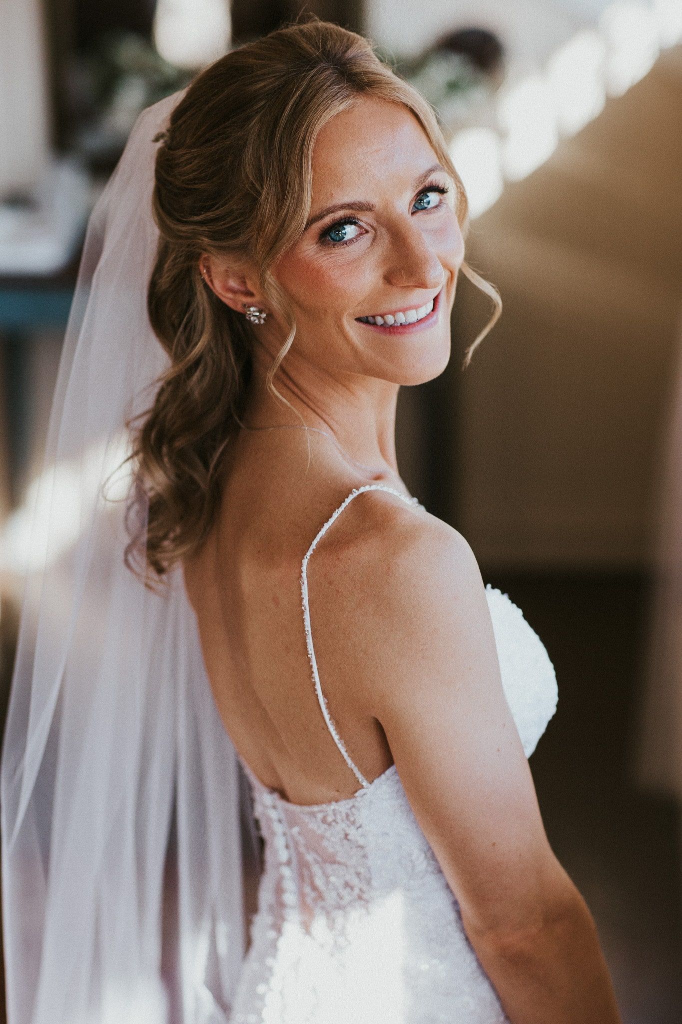 A woman in a wedding dress and veil is smiling.