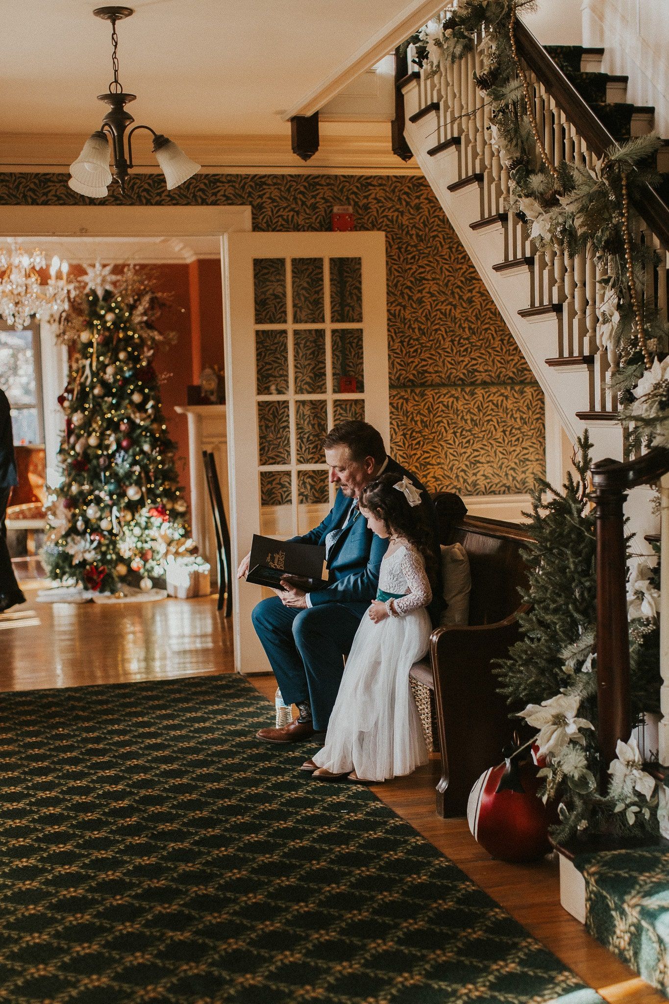 A man and a little girl are sitting in front of a christmas tree.