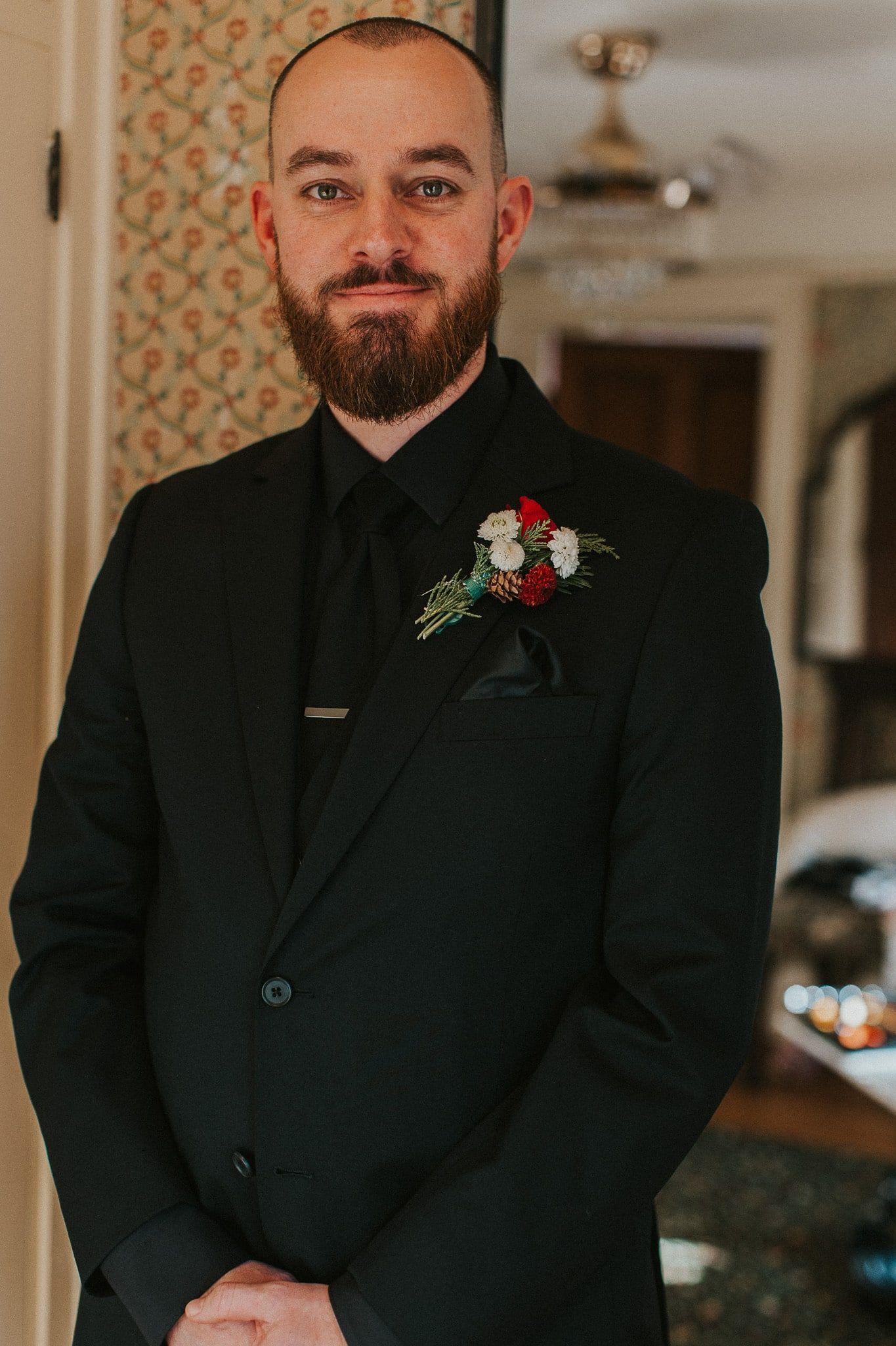 A man with a beard is wearing a black suit and tie.
