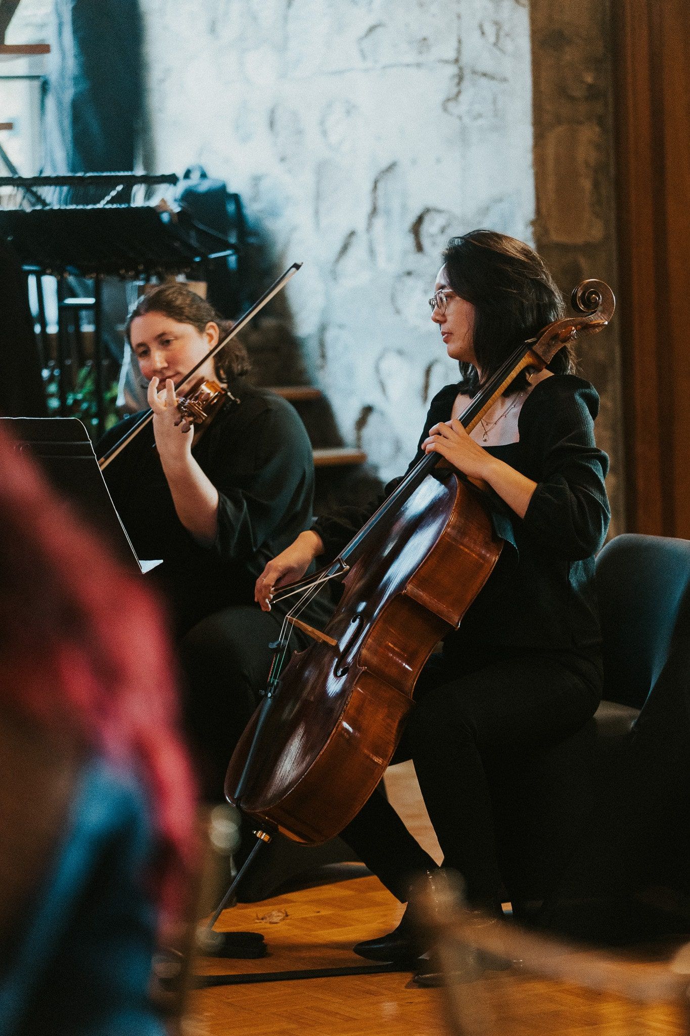Two women are playing violins and cello in a room.