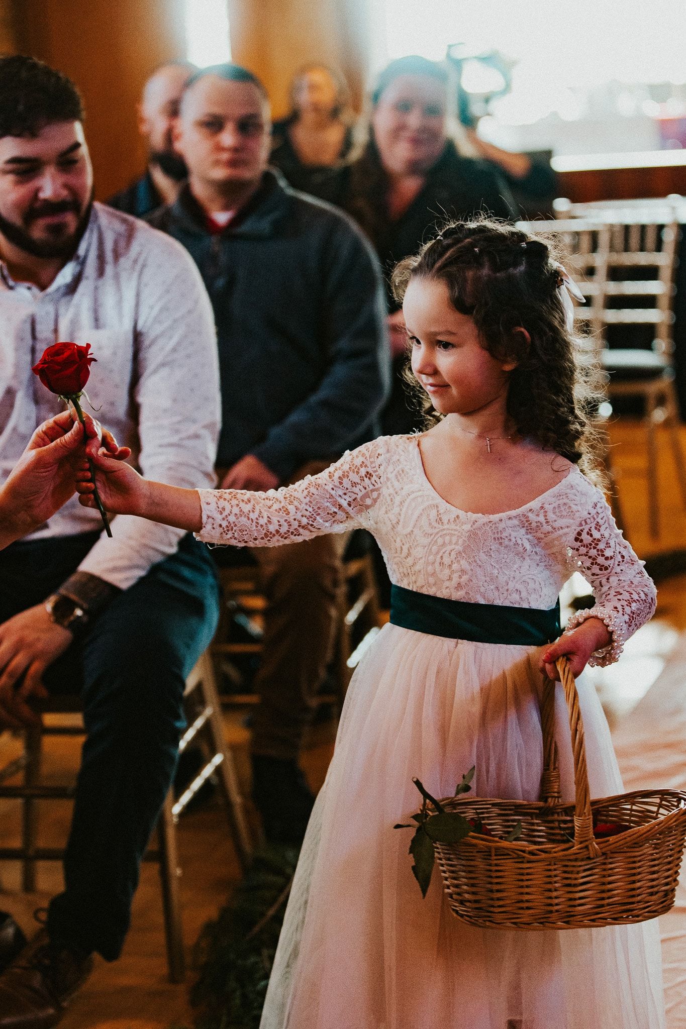 A flower girl is holding a rose in her hand while walking down the aisle at a wedding.