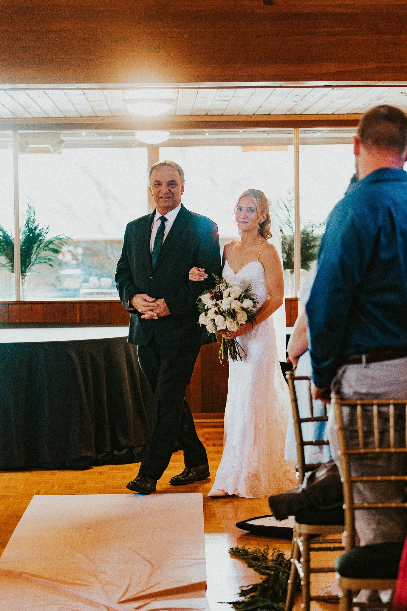 Bride and her father walking down aisle, sunlight streams in.  Bride in white dress, holding bouquet.  Father in suit.