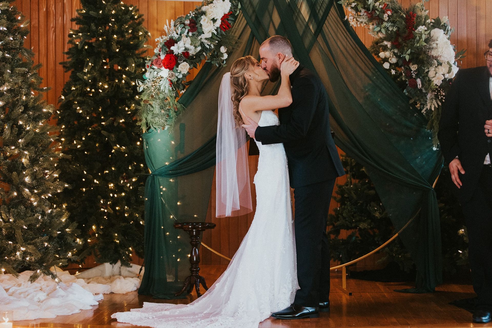 A bride and groom are kissing at their wedding ceremony in front of christmas trees.