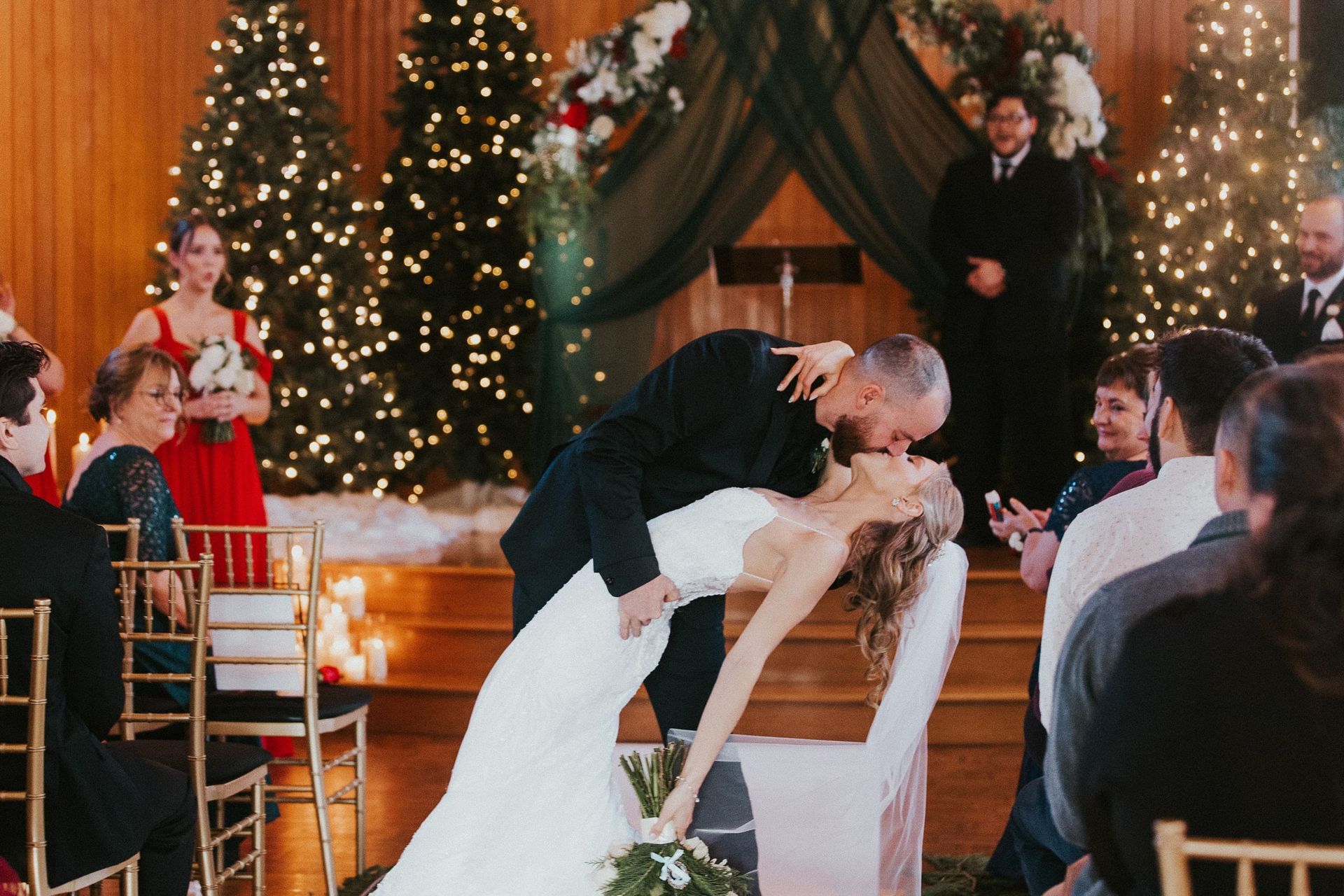 A bride and groom kissing at their wedding ceremony in front of christmas trees.