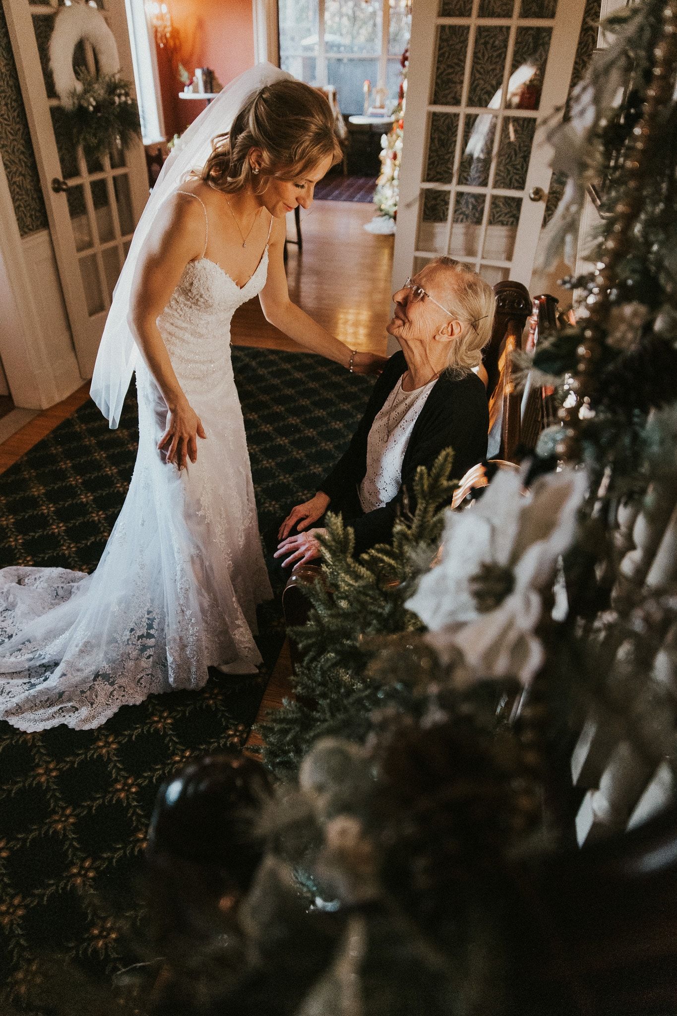 A bride in a wedding dress is standing next to an older woman in a living room.
