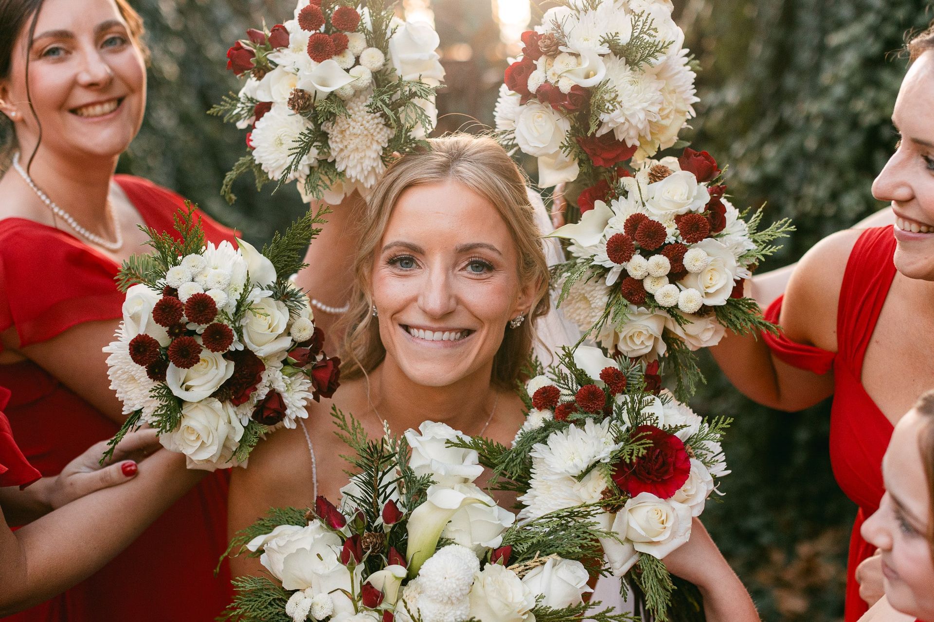 A bride and her bridesmaids are holding bouquets of red and white flowers.