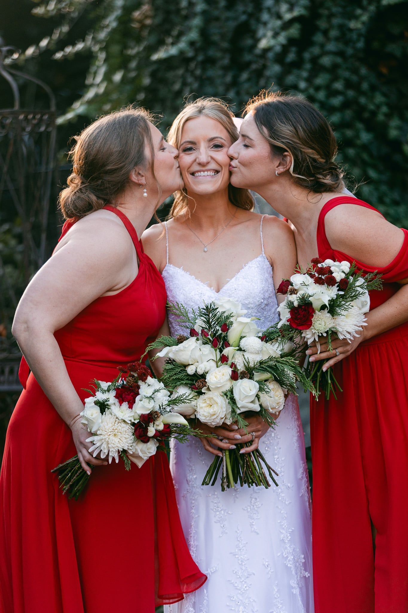 The bride and her bridesmaids are kissing the bride on the cheek.