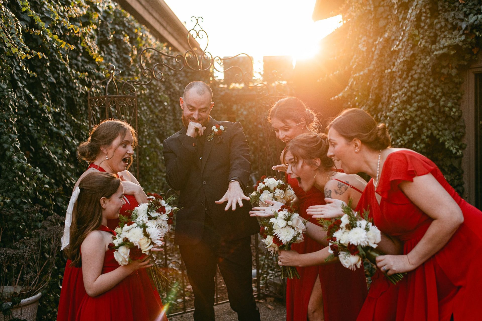 A bride and groom are standing next to their bridesmaids in red dresses.