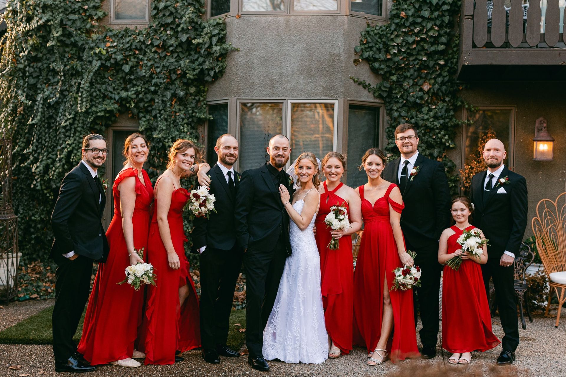 A bride and groom are posing for a picture with their wedding party in front of a building.
