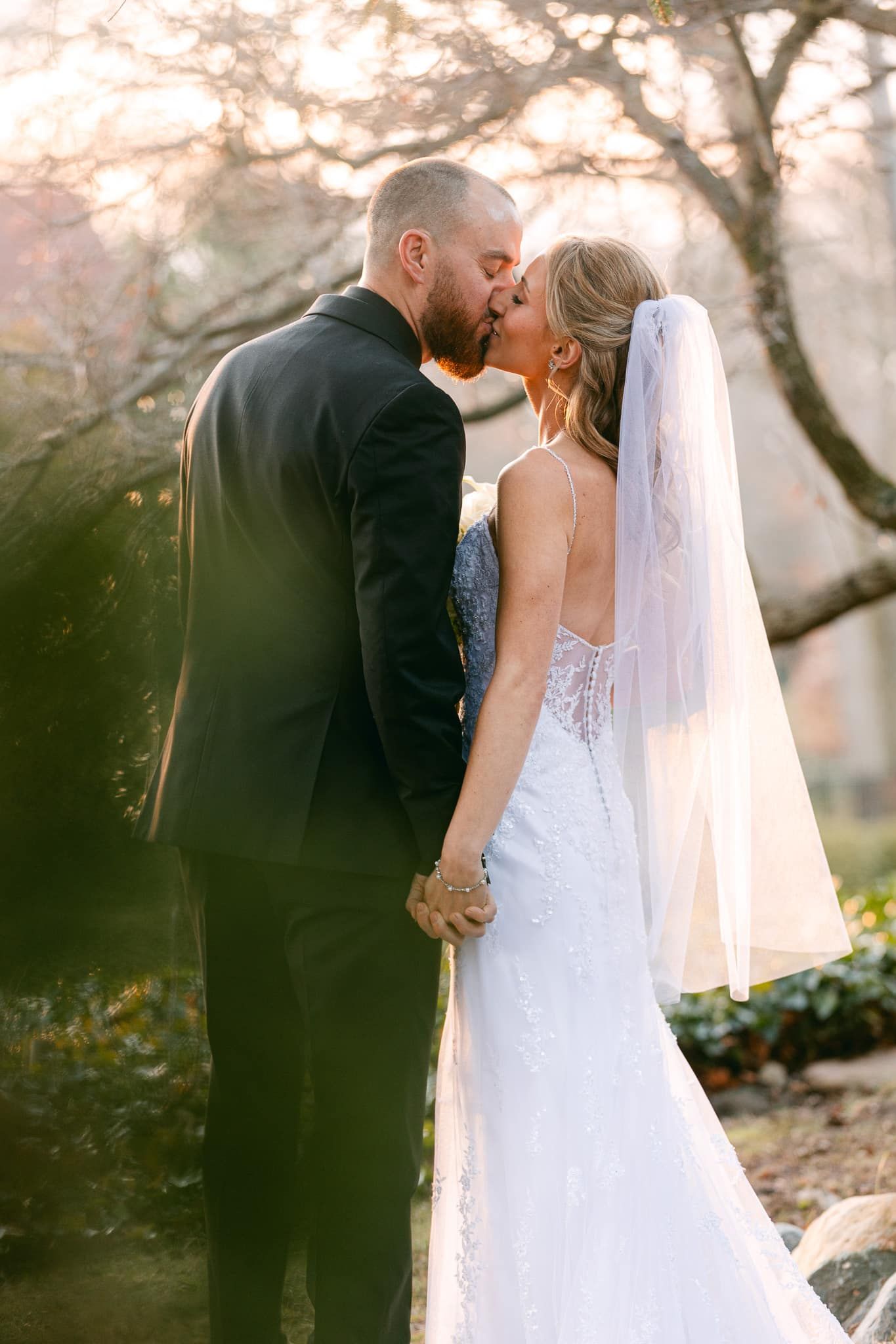 A bride and groom are kissing in front of a tree.
