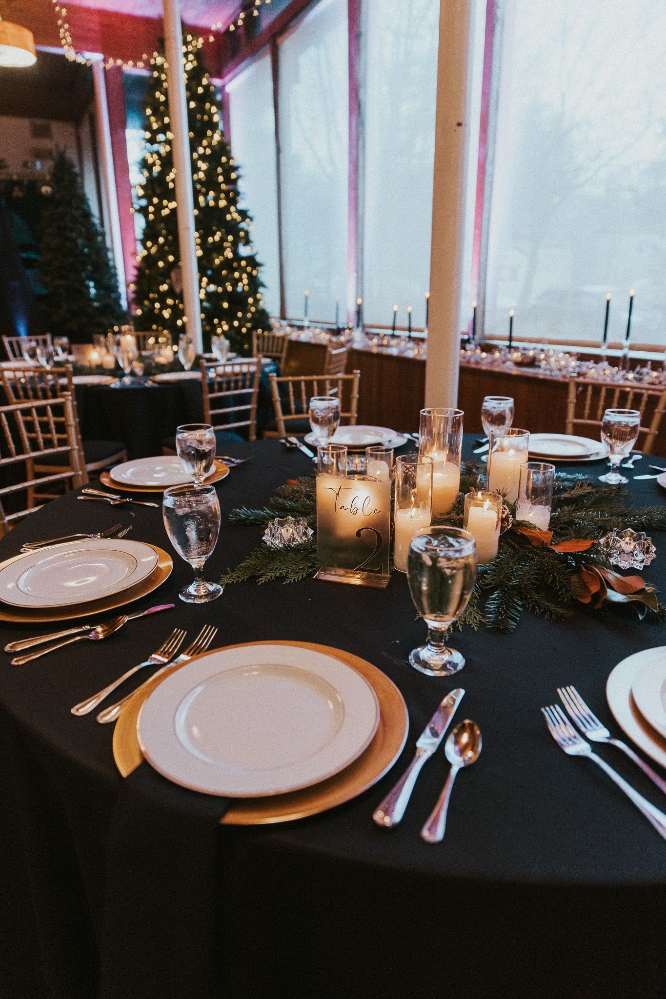 A table with plates , candles , utensils and a christmas tree in the background.
