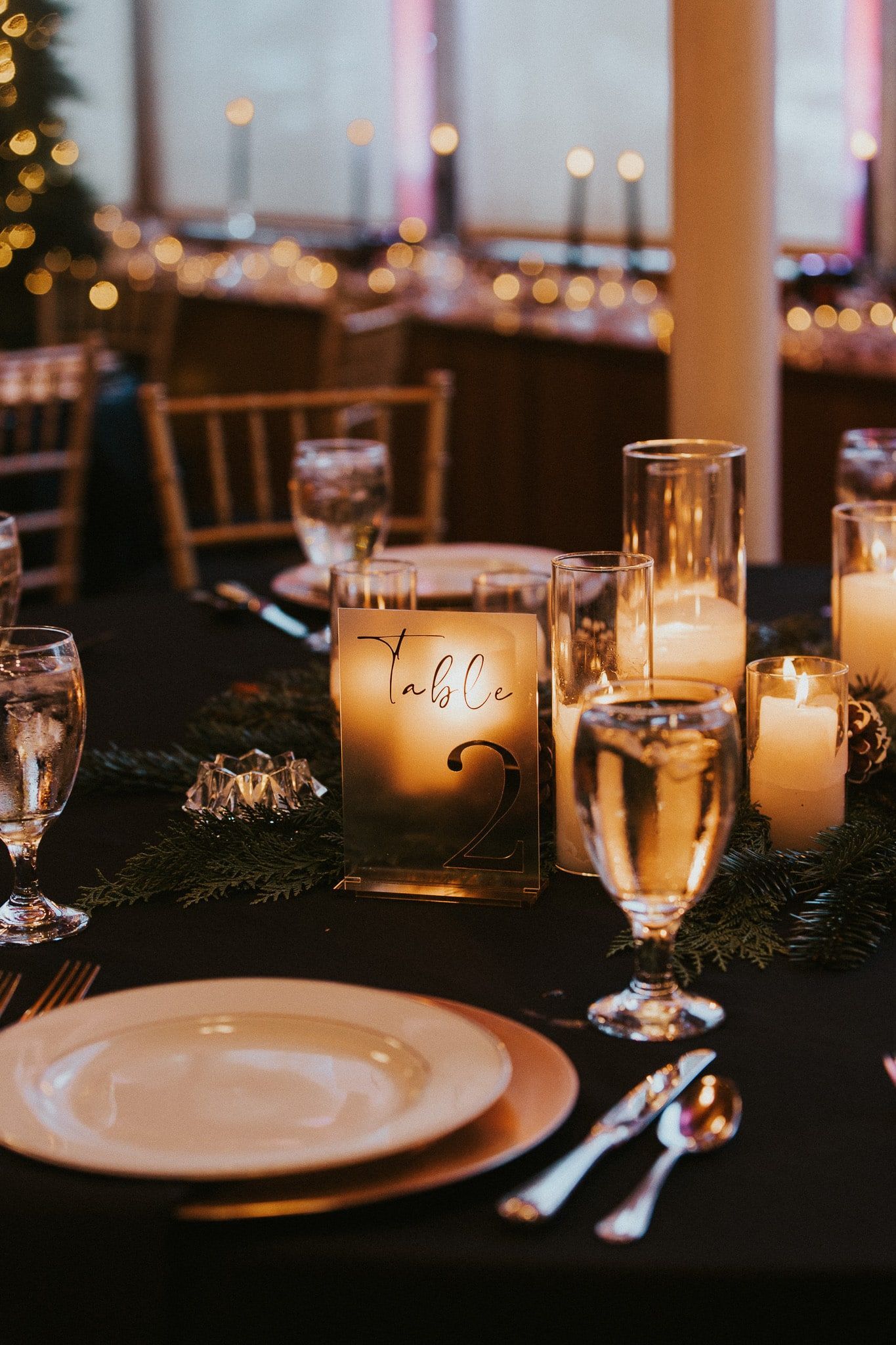 A table with plates , glasses , candles and a christmas tree in the background.