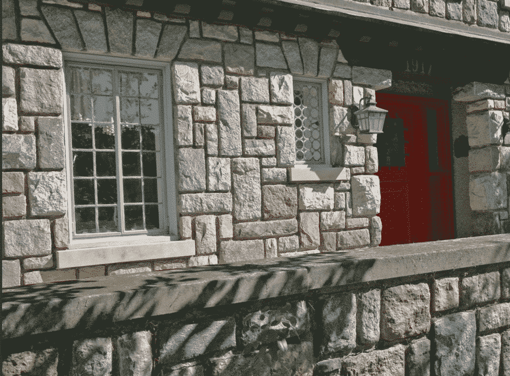Stone building facade with red door, windows, and decorative stone wall in sunlight.