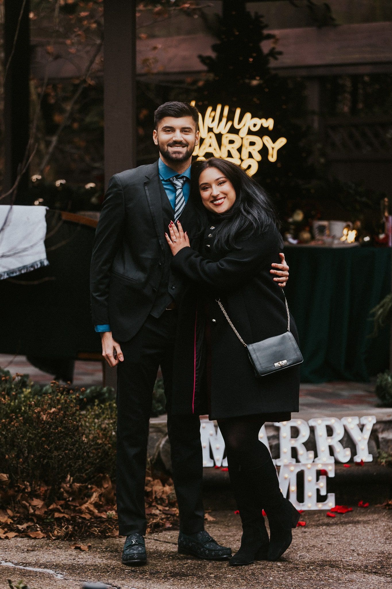 A man in a suit and tie is hugging a woman in a black coat.
