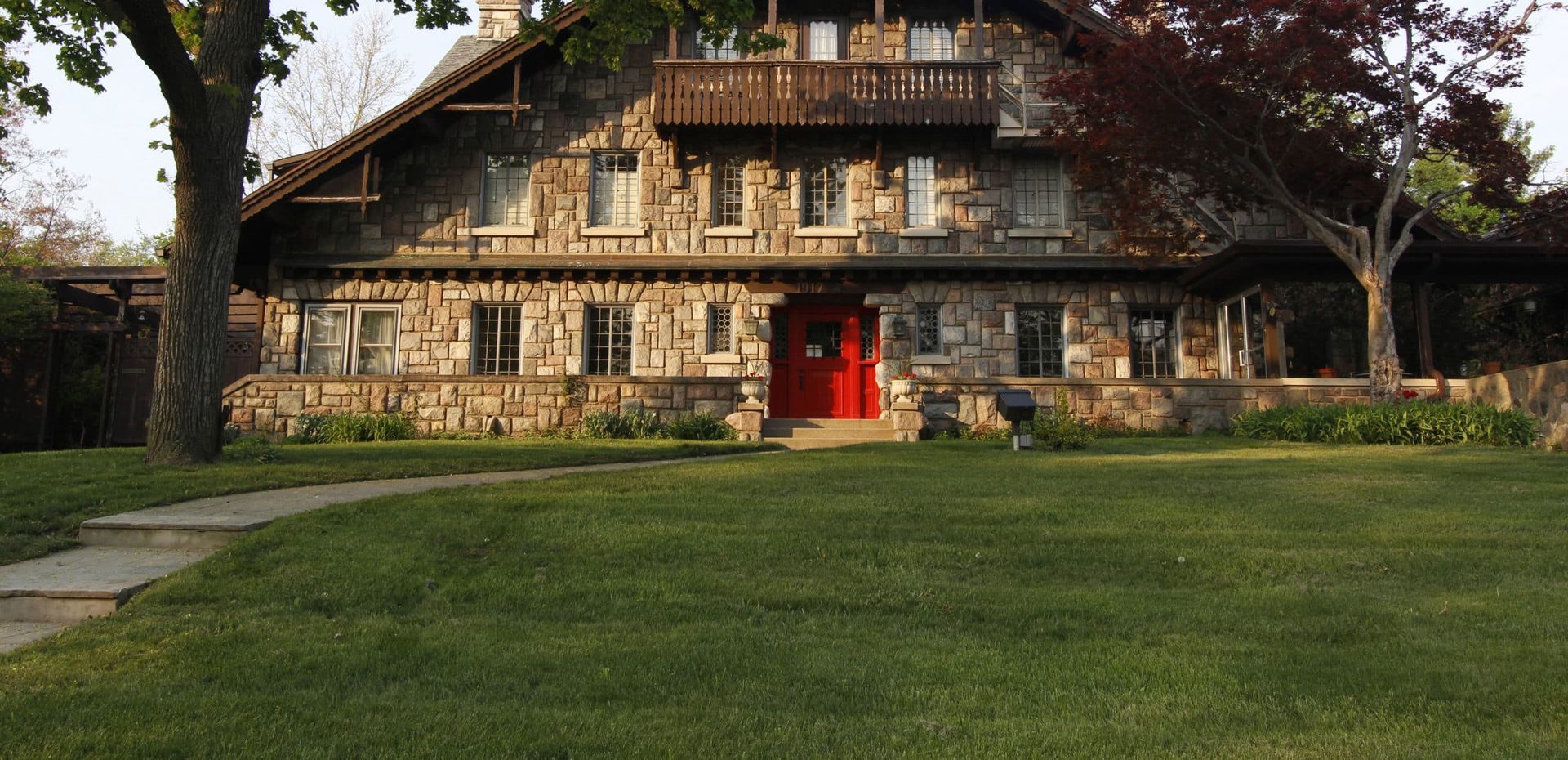 A large stone house with a red door and a lush green lawn in front of it.