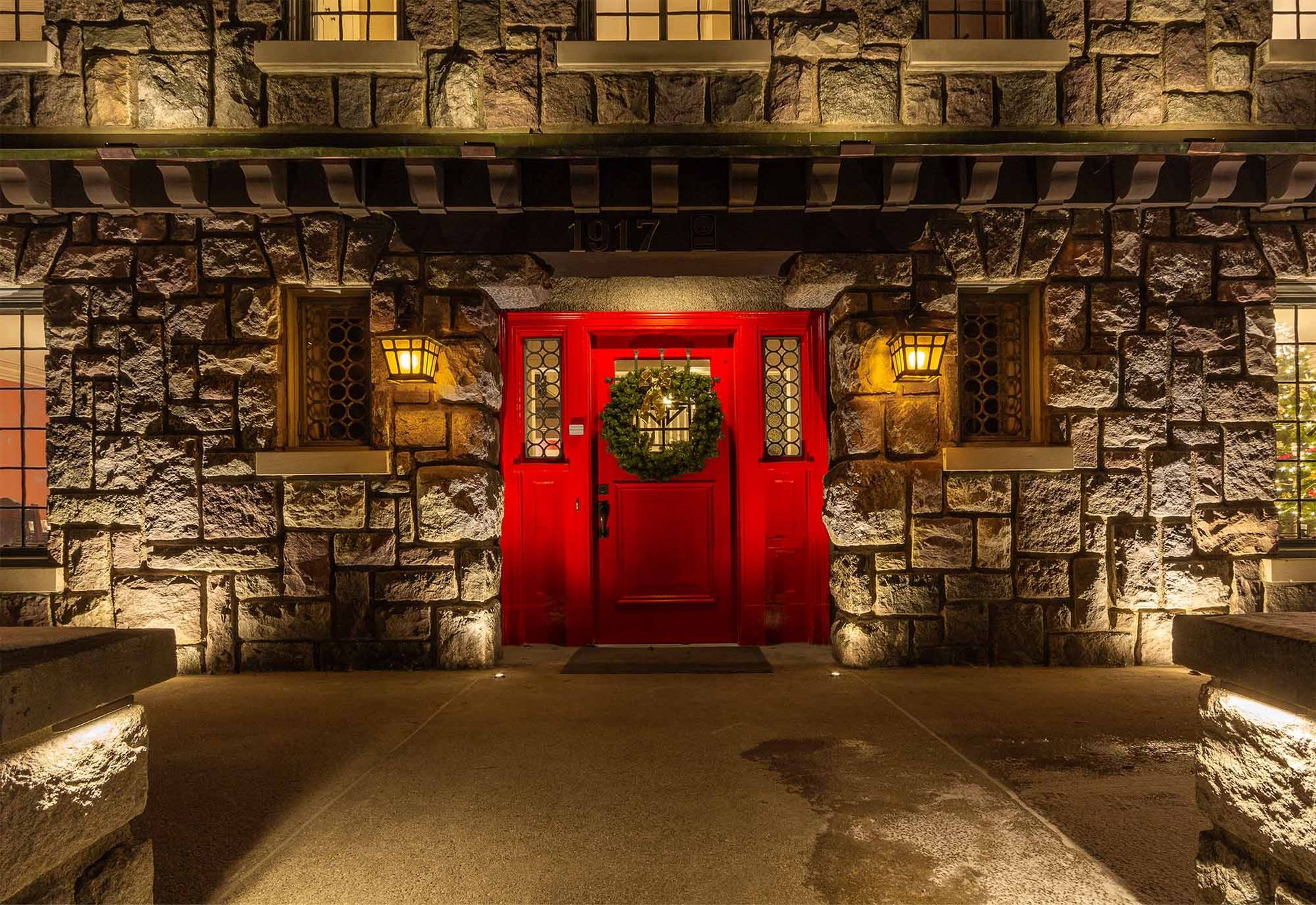 A red door with a wreath on it is on a stone building.