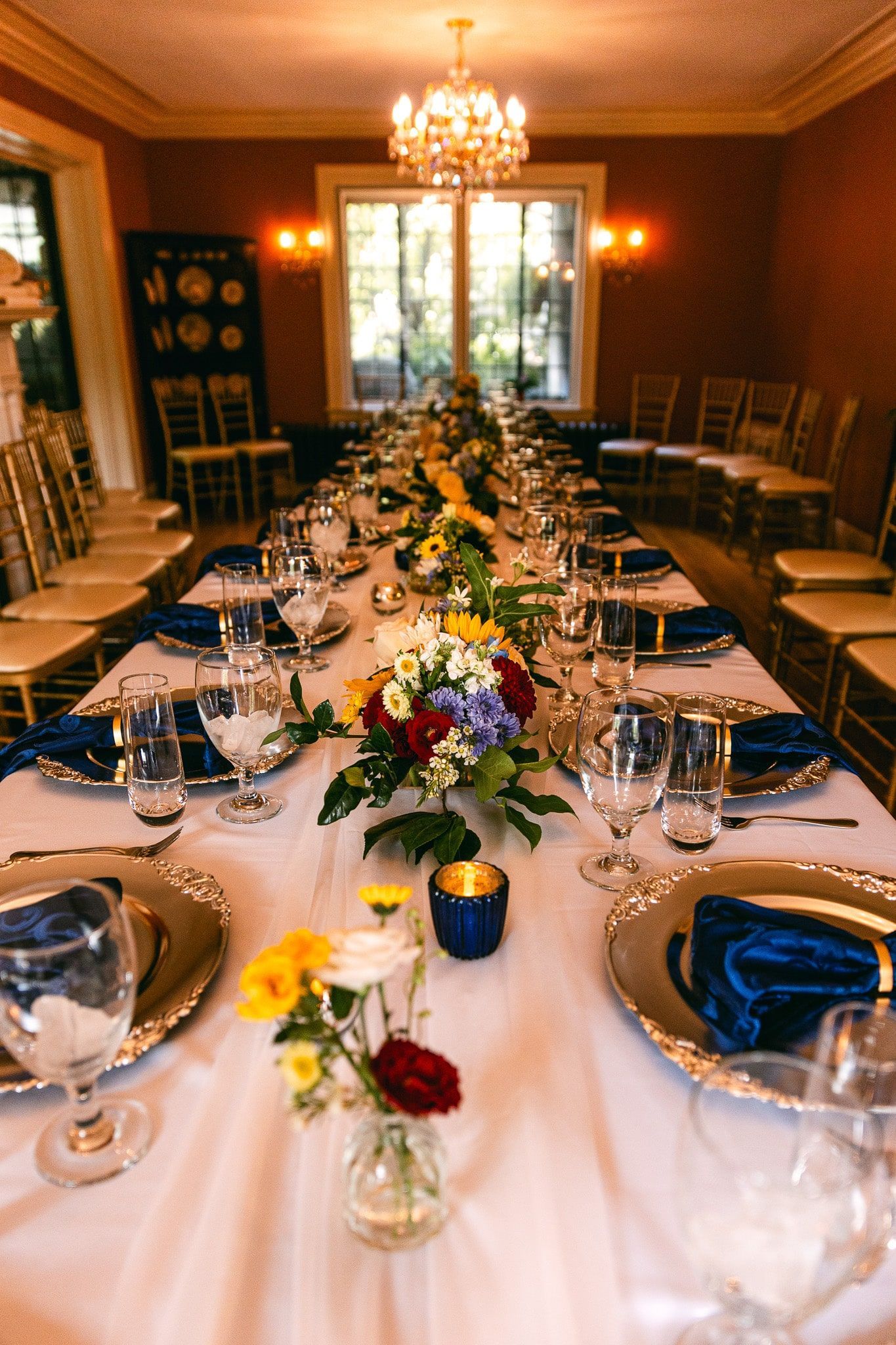 A long table with plates , glasses , and flowers on it.